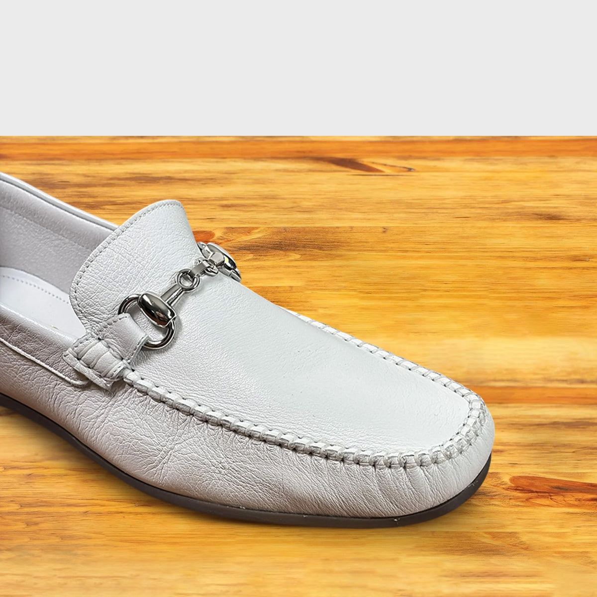 White loafer shoe with silver buckle on a wooden surface