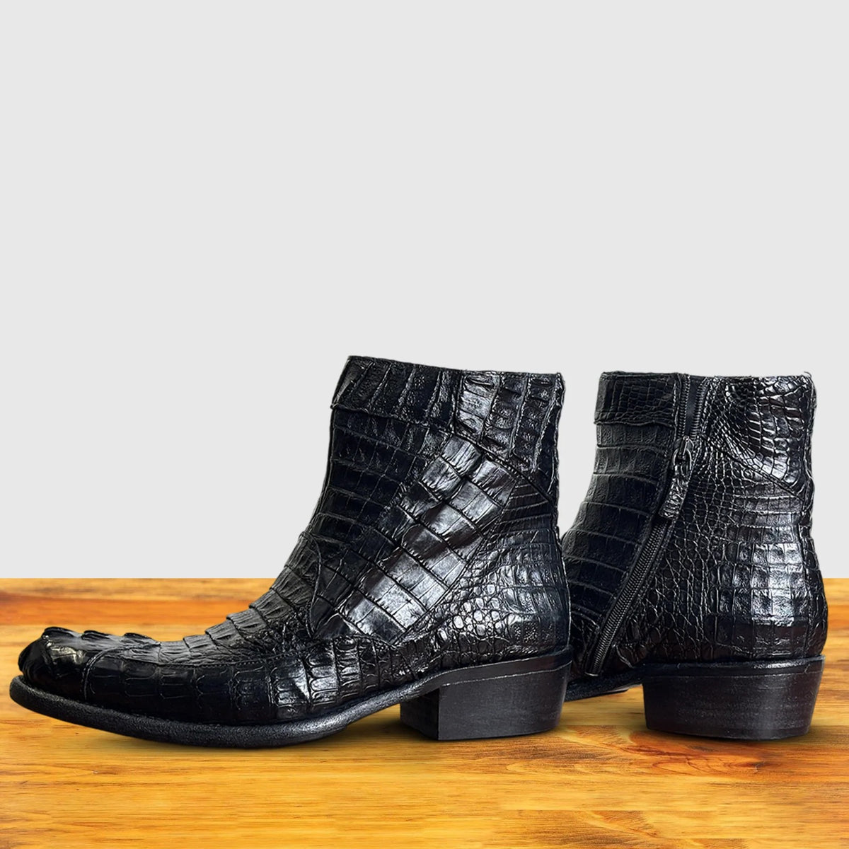Side view of Black crocodile western boot on a wooden surface with a light gray background