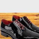 Pair of Black patent leather shoe with red laces on a wooden surface