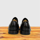 A pair of Dark Brown leather dress shoes shown from the back, resting on a wooden surface against a light gray background.