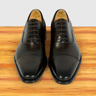 A pair of Dark Brown leather cap-toe oxford shoes with laces, displayed on wooden shoe trees and set on a wooden surface against a light gray background.