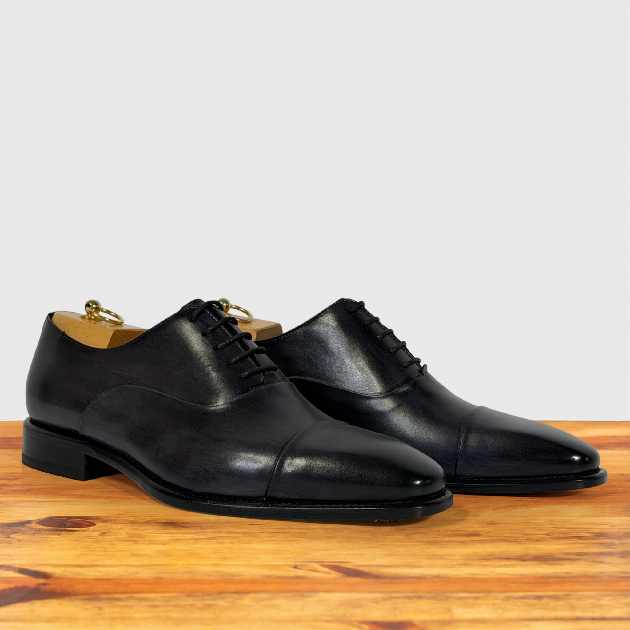 A pair of Gray leather cap-toe oxford dress shoes, displayed on a wooden surface against a light gray background.