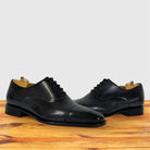 A pair of Gray leather cap-toe oxford dress shoes with black laces, displayed on a wooden surface against a light gray background.