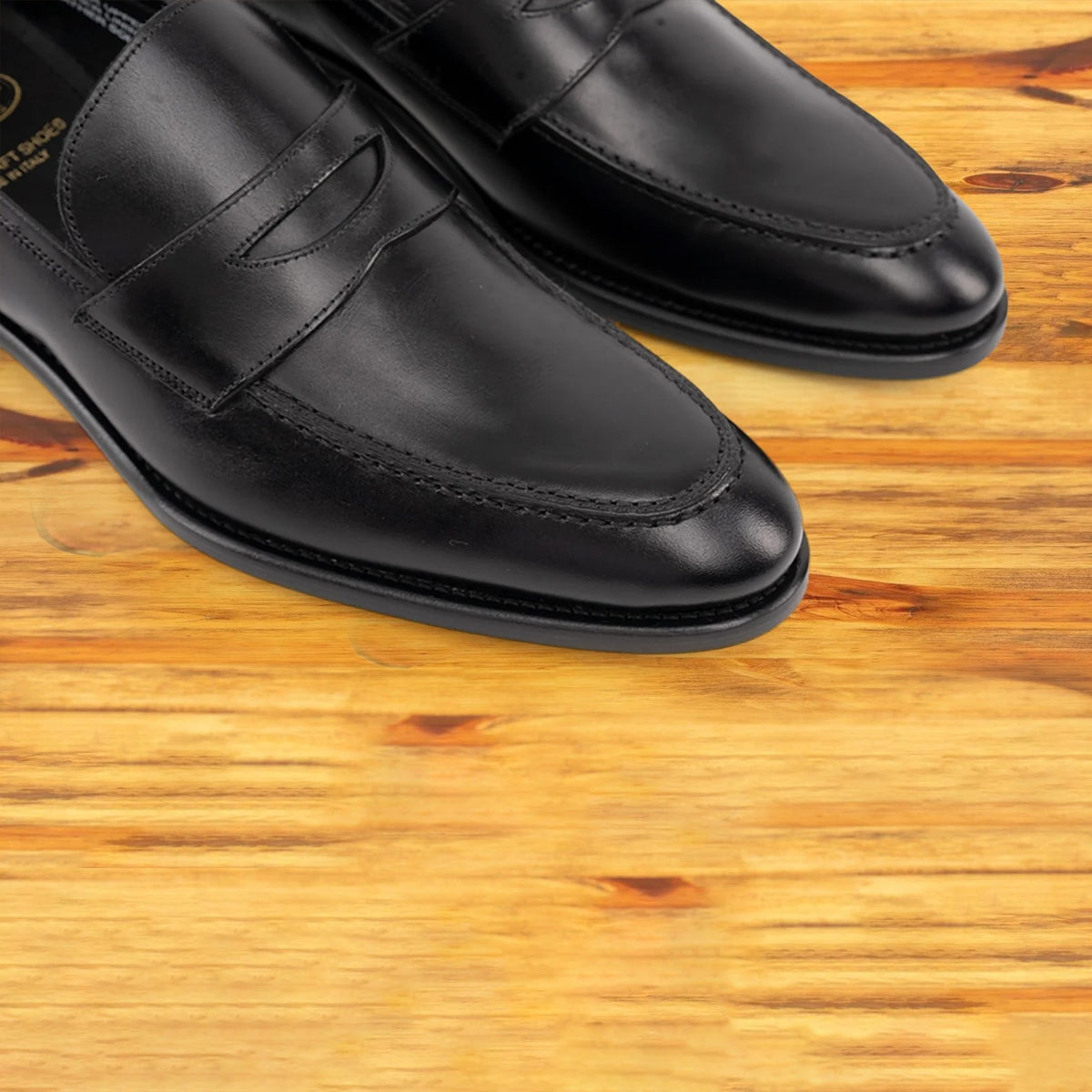 A Pair of black Italian leather dress loafer with a penny strap, on a wooden surface.
