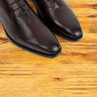 Pair of burgundy Italian wholecut Oxford shoe with laces on a wooden surface.