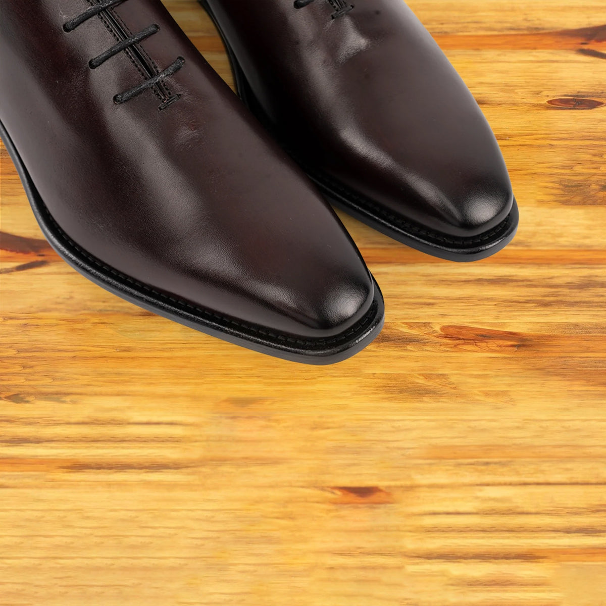 Pair of burgundy Italian wholecut Oxford shoe with laces on a wooden surface.