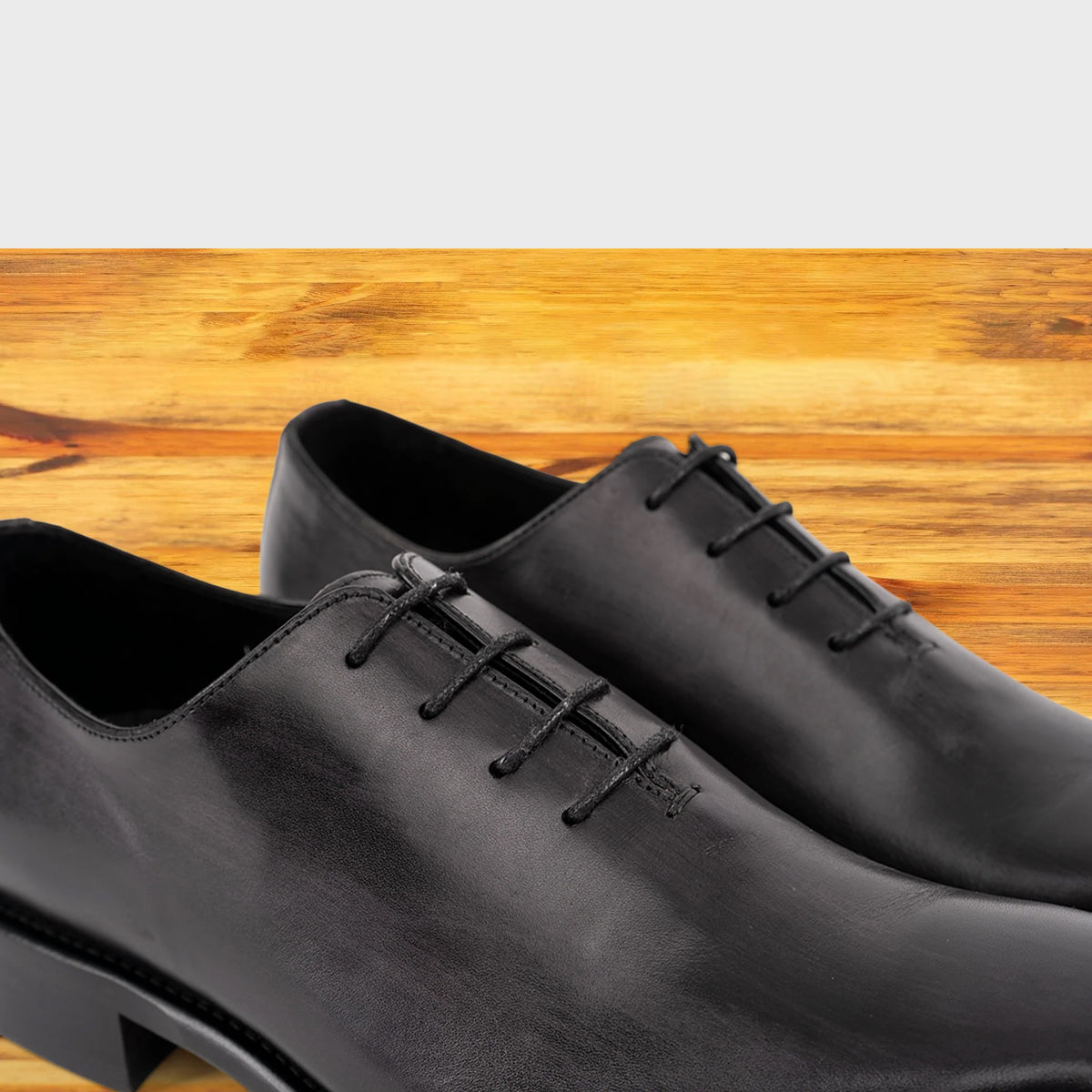 A Pair of Graphite Italian wholecut Oxford shoe with laces on a wooden surface.
