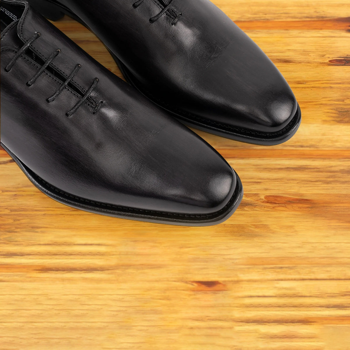 A Pair of Graphite Italian wholecut Oxford shoe with laces on a wooden surface.