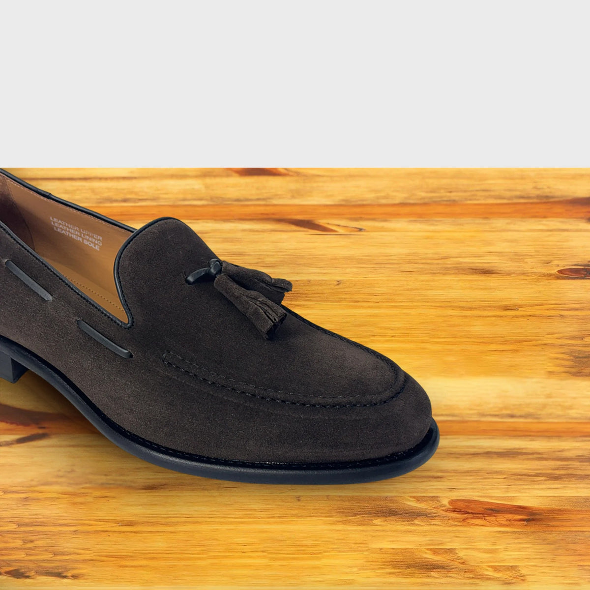 A  Dusty Brown color loafer with a tassel  placed on a wooden surface.