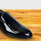 Black patent leather loafer on a wooden surface