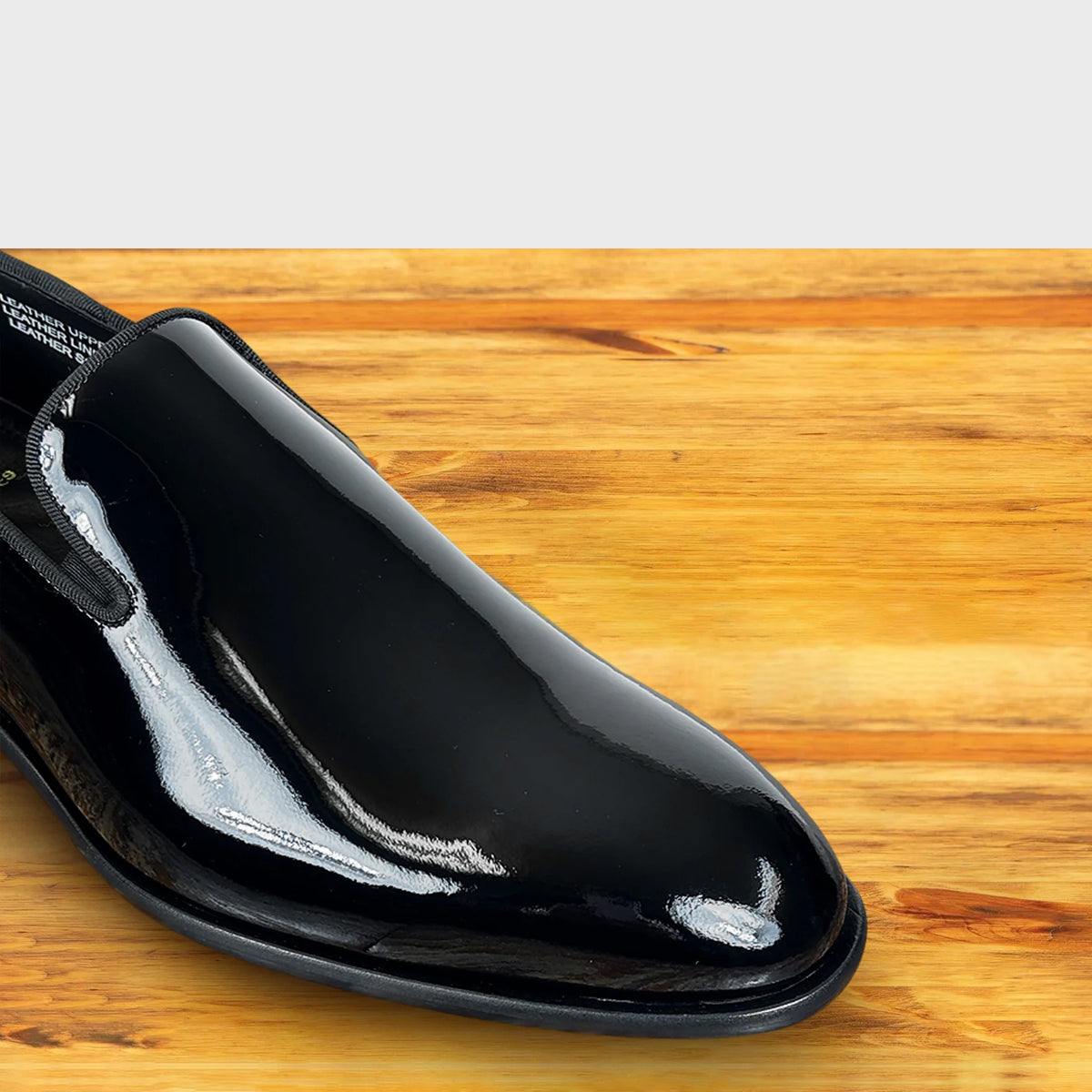 Black patent leather loafer on a wooden surface