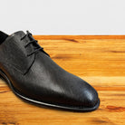 Black leather dress shoe on a wooden surface