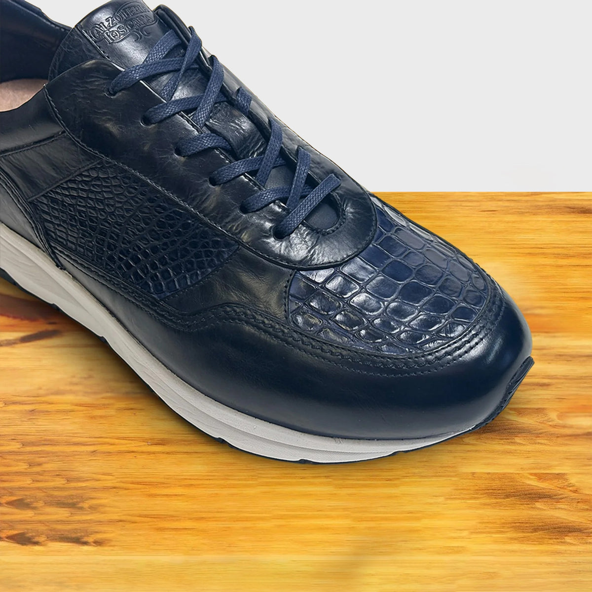 Blue sneaker with a white sole on a wooden surface