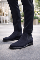 Navy blue suede boots worn with black pants on a blurred outdoor background