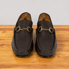A pair of dark brown  leather penny loafers with gold buckle on a wooden surface against a neutral light gray background.
