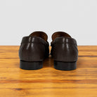 A pair of dark brown leather loafers shown from the back, resting on a wooden surface against a light gray background.