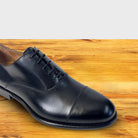Close up of a Black leather dress shoe on a wooden surface