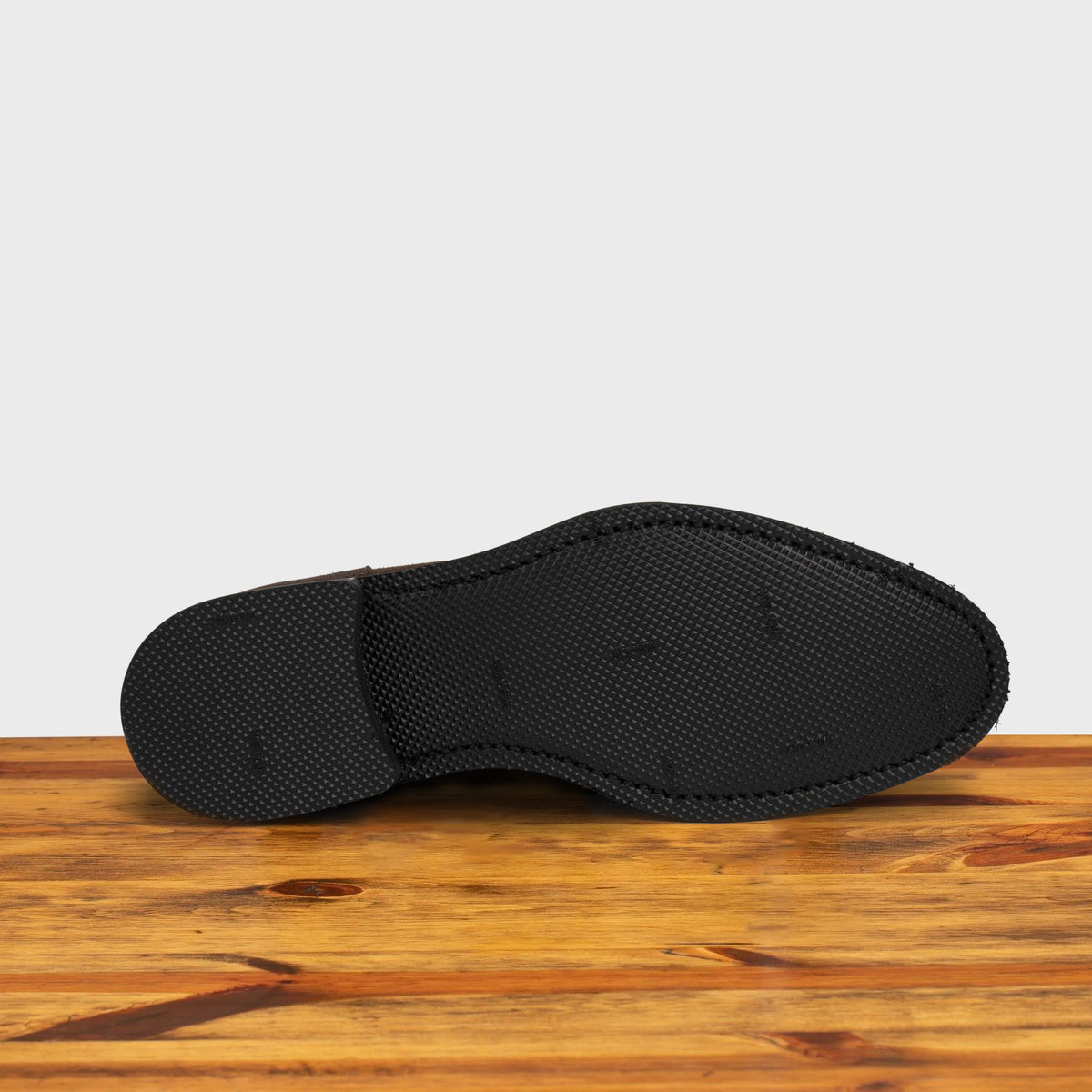 Outsole of the Dusty Brown suede dress shoe on a wooden surface with a light gray background