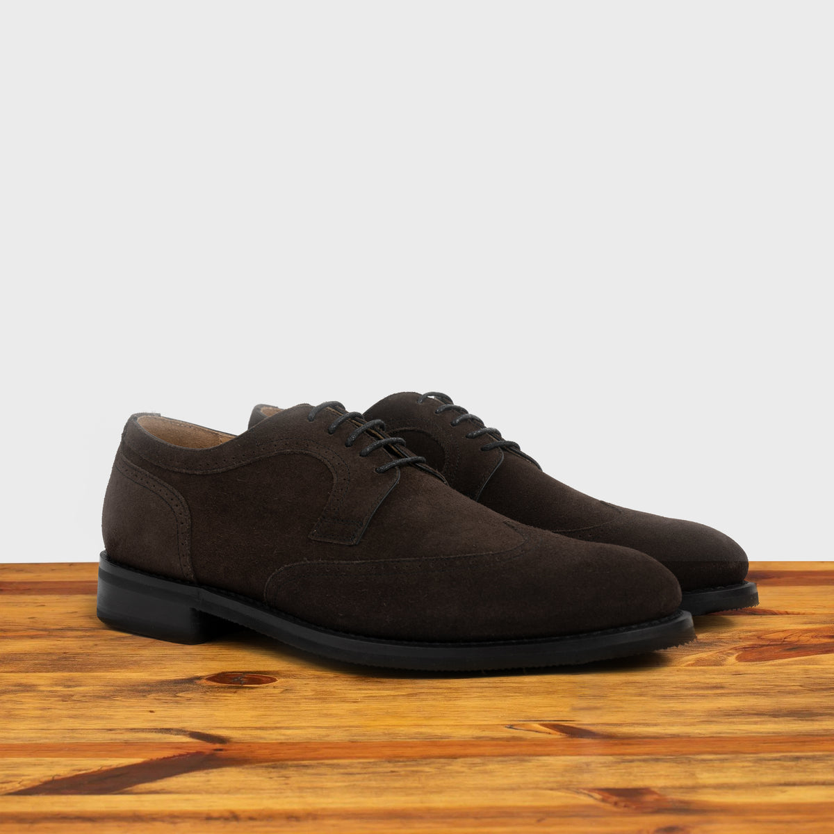 Pair of Dusty Brown suede dress shoe on a wooden surface with a light gray background
