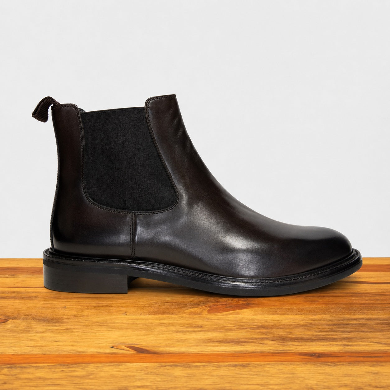 Black leather Chelsea boot on a wooden surface with a light gray background