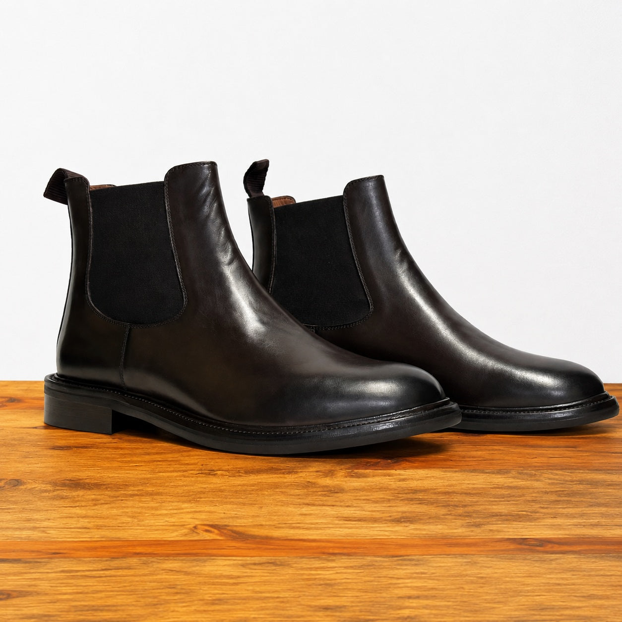Pair of black leather Chelsea boots on a wooden surface with a light gray background