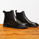 Pair of black leather Chelsea boots on a wooden surface with a light gray background