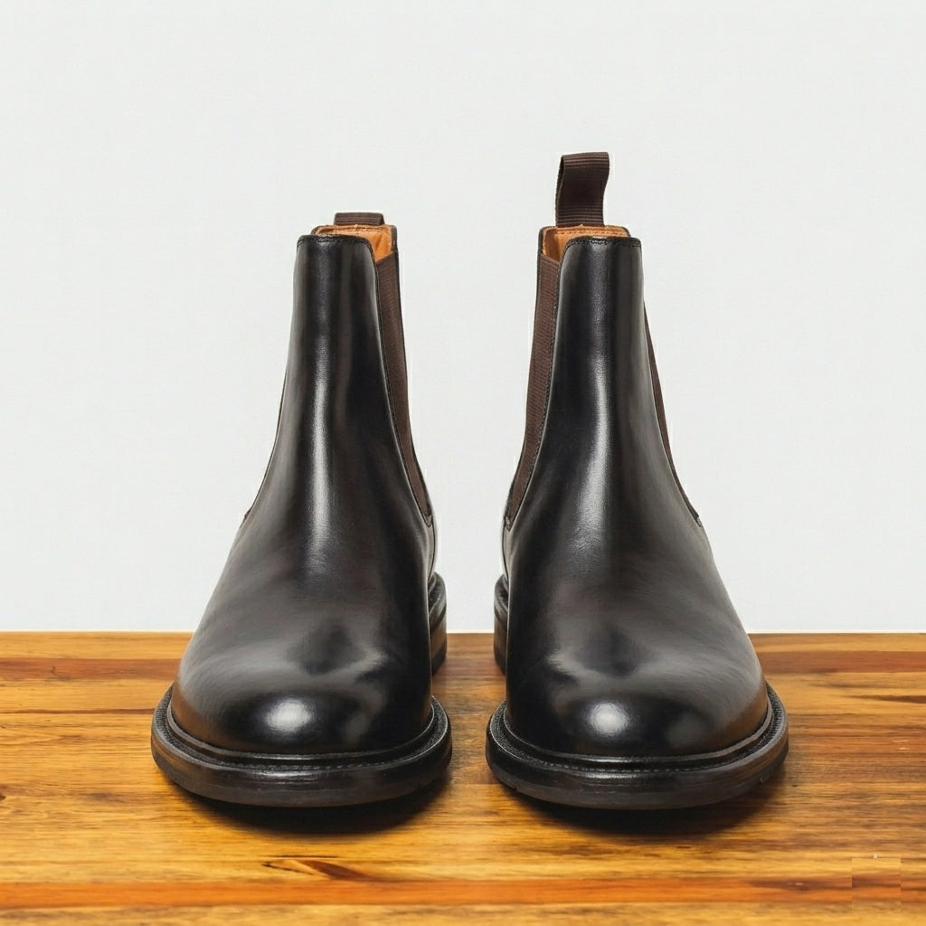 Pair of Dark Brown color leather boots on a wooden surface with a light gray background