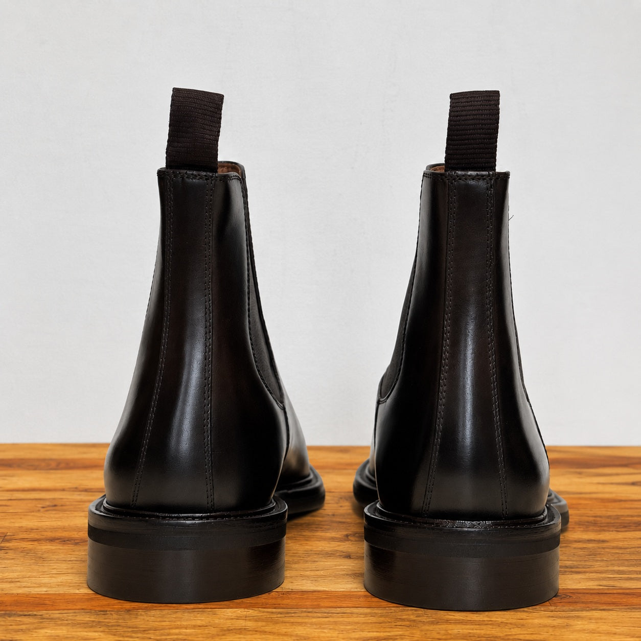 Pair of Dark Brown color leather boots on a wooden surface with a light gray background