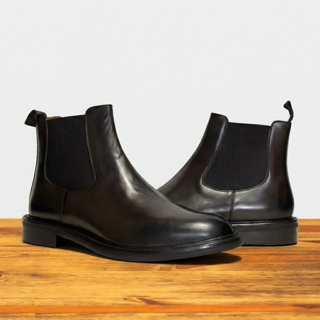 Pair of Dark Brown color leather Chelsea boots on a wooden surface with a light gray background