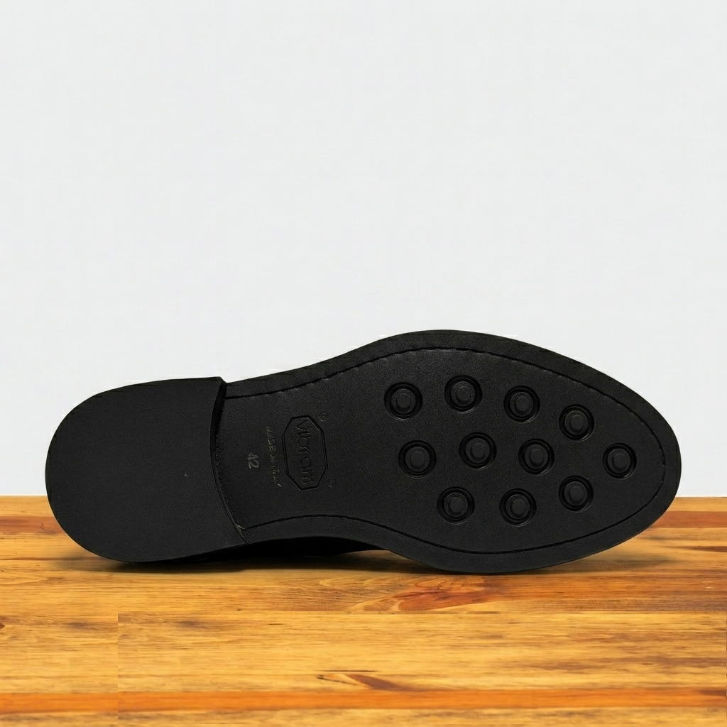 Dark Brown colored Boot black out sole with tread pattern on a wooden surface