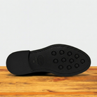Black shoe sole with tread pattern on a wooden surface