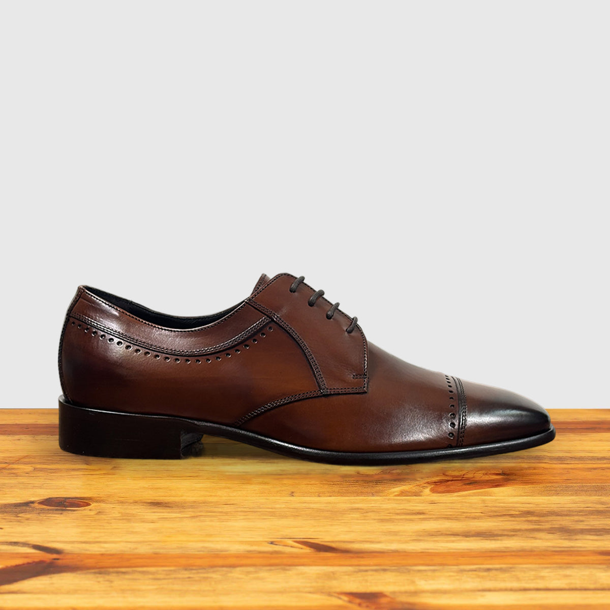 Mahogany leather dress shoe on a wooden surface with a light gray background