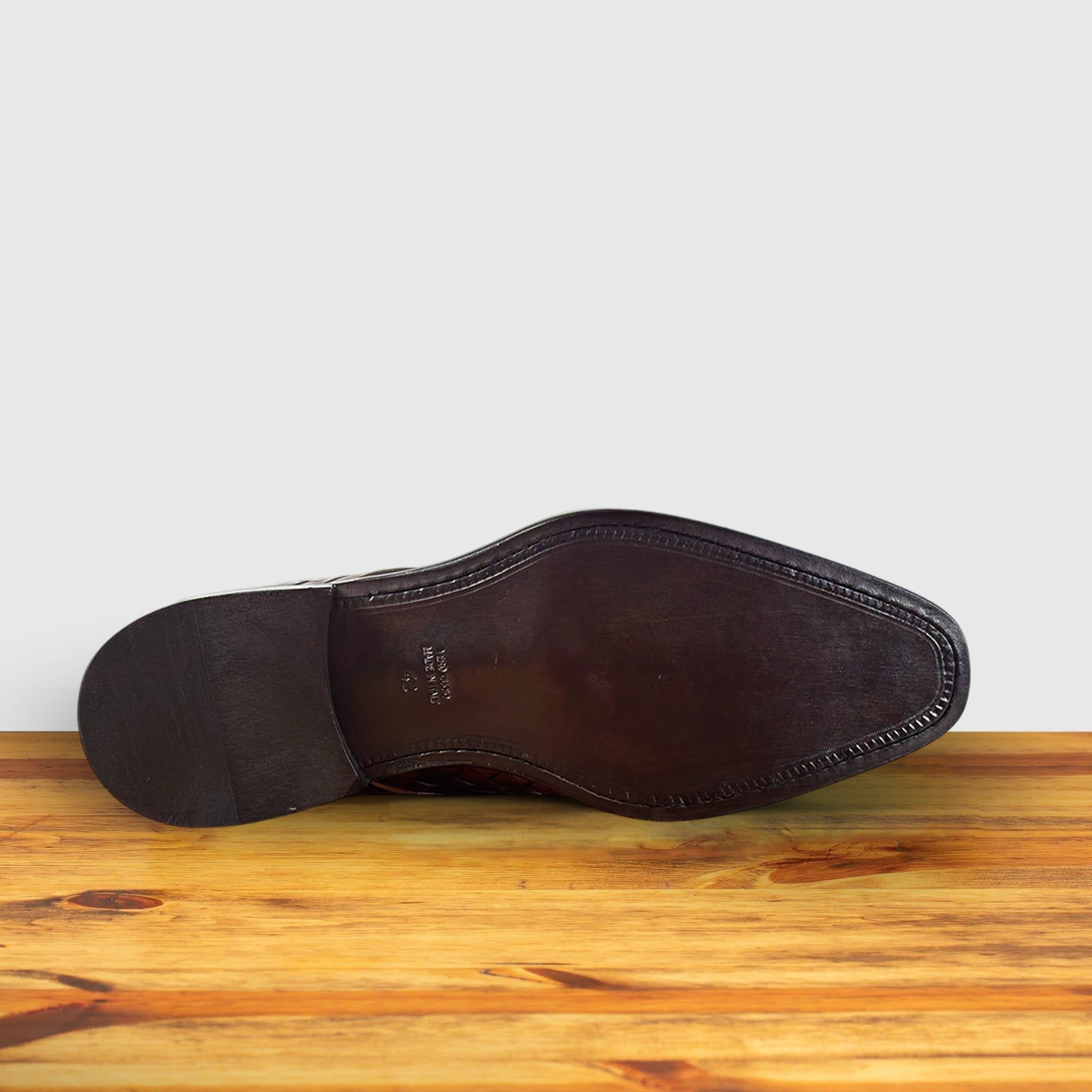 Outsole of the woven leather shoe on a wooden surface with a light gray background