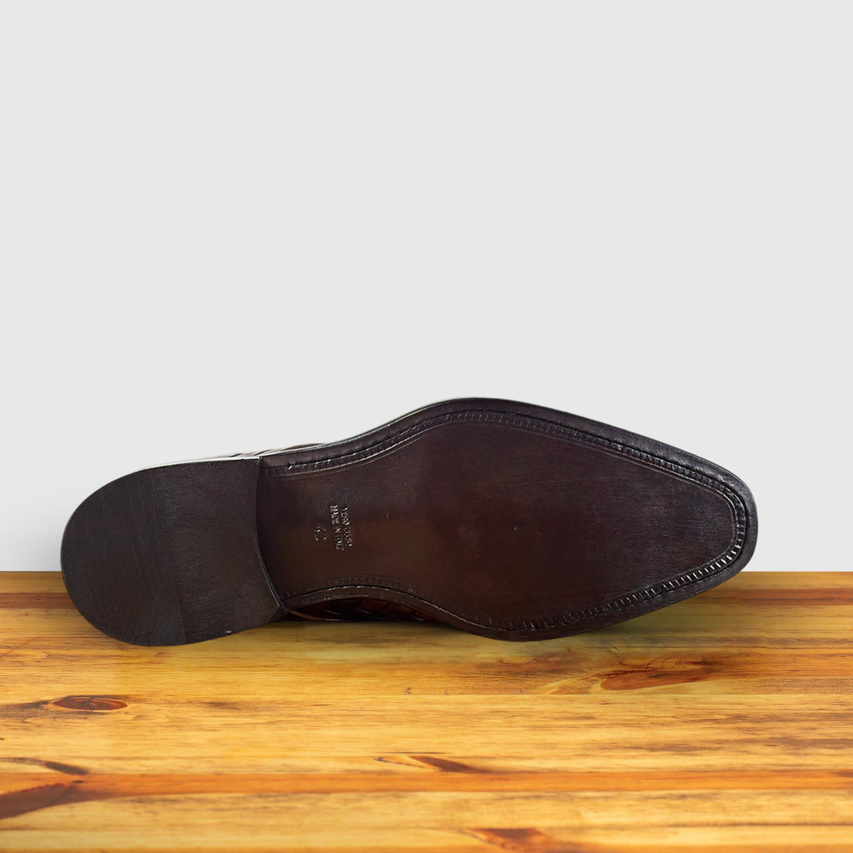 Outsole of the Mahogany woven leather shoe on a wooden surface with a light gray background