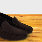 A pair of brown suede moccasin loafers resting on a light-colored wooden surface.