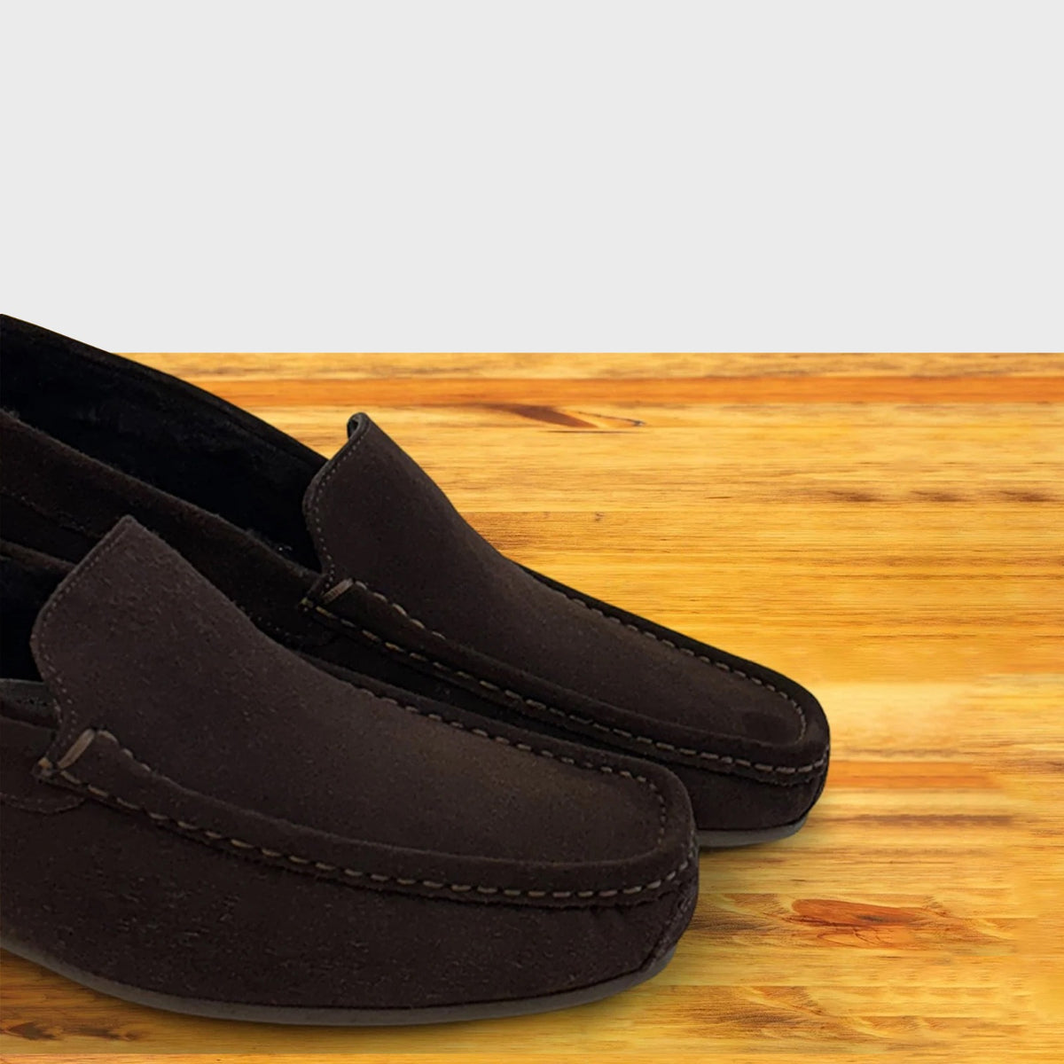 A pair of brown suede moccasin loafers resting on a light-colored wooden surface.