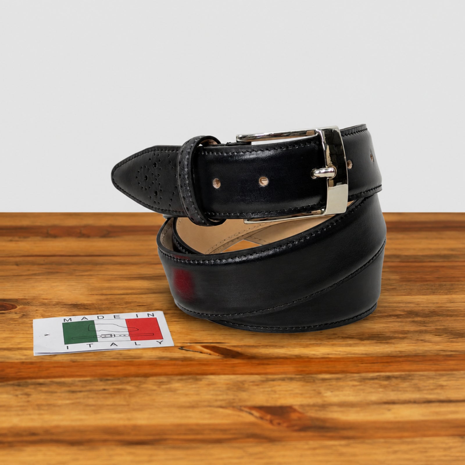 A Graphite leather belt with a silver buckle, coiled on a wooden surface next to a small 'Made in Italy' card.