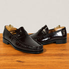 A pair of burgundy leather penny loafers with decorative stitching and low black heels, displayed on a wooden surface with wooden shoe trees visible inside.