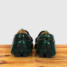 A pair of Emerald Green crocodile-embossed leather shoes viewed from the back, resting on a wooden surface against a light gray background.