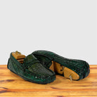 A pair of Emerald Green crocodile-embossed leather loafers resting on a wooden surface against a light gray background.
