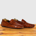 A pair of Burnt Orange crocodile-embossed leather penny loafers, displayed on a wooden surface against a light gray background.