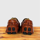A pair of Burnt Orange crocodile-embossed leather loafers shown from the back, resting on a wooden surface against a light gray background.