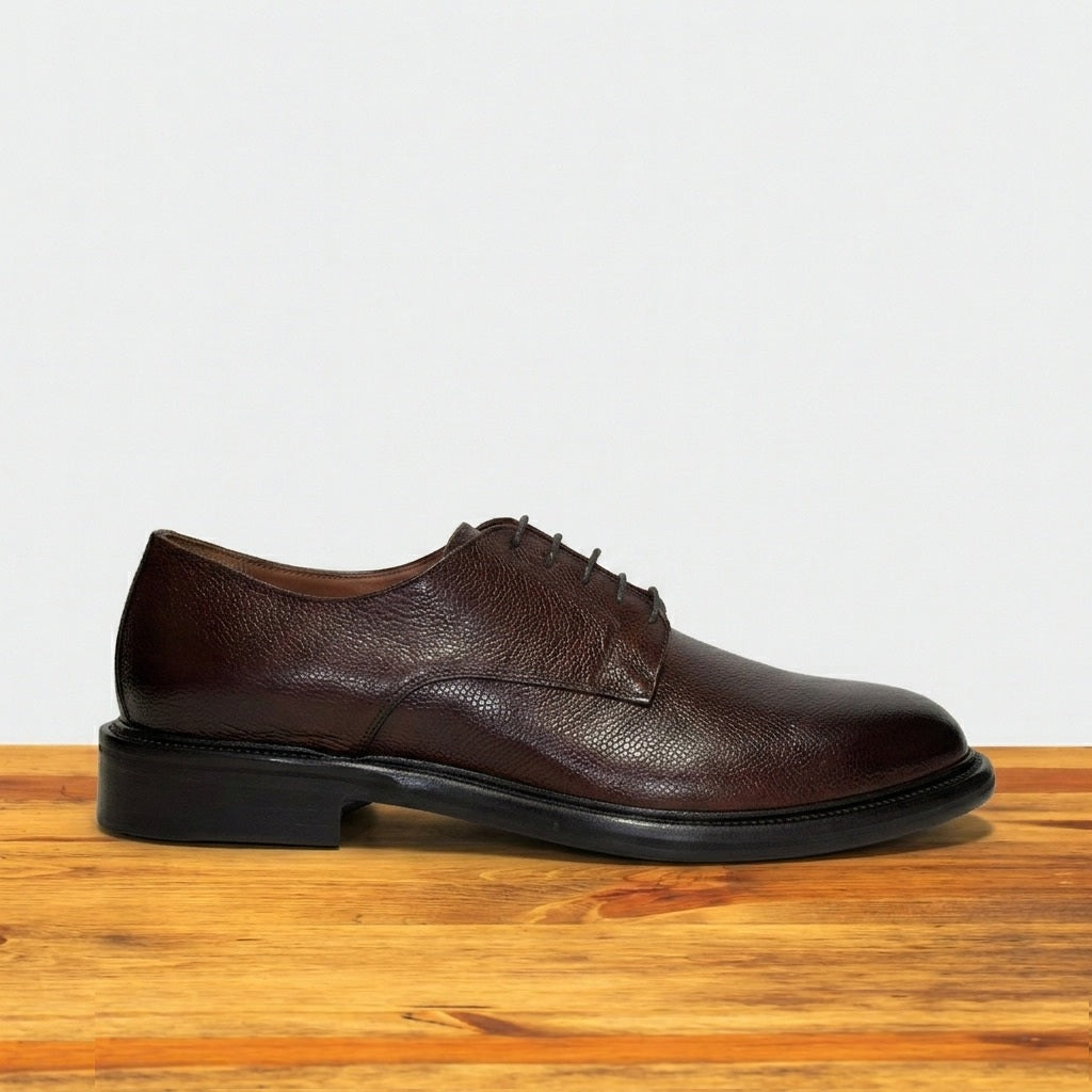Tobacco leather shoe on a wooden surface with a light gray background