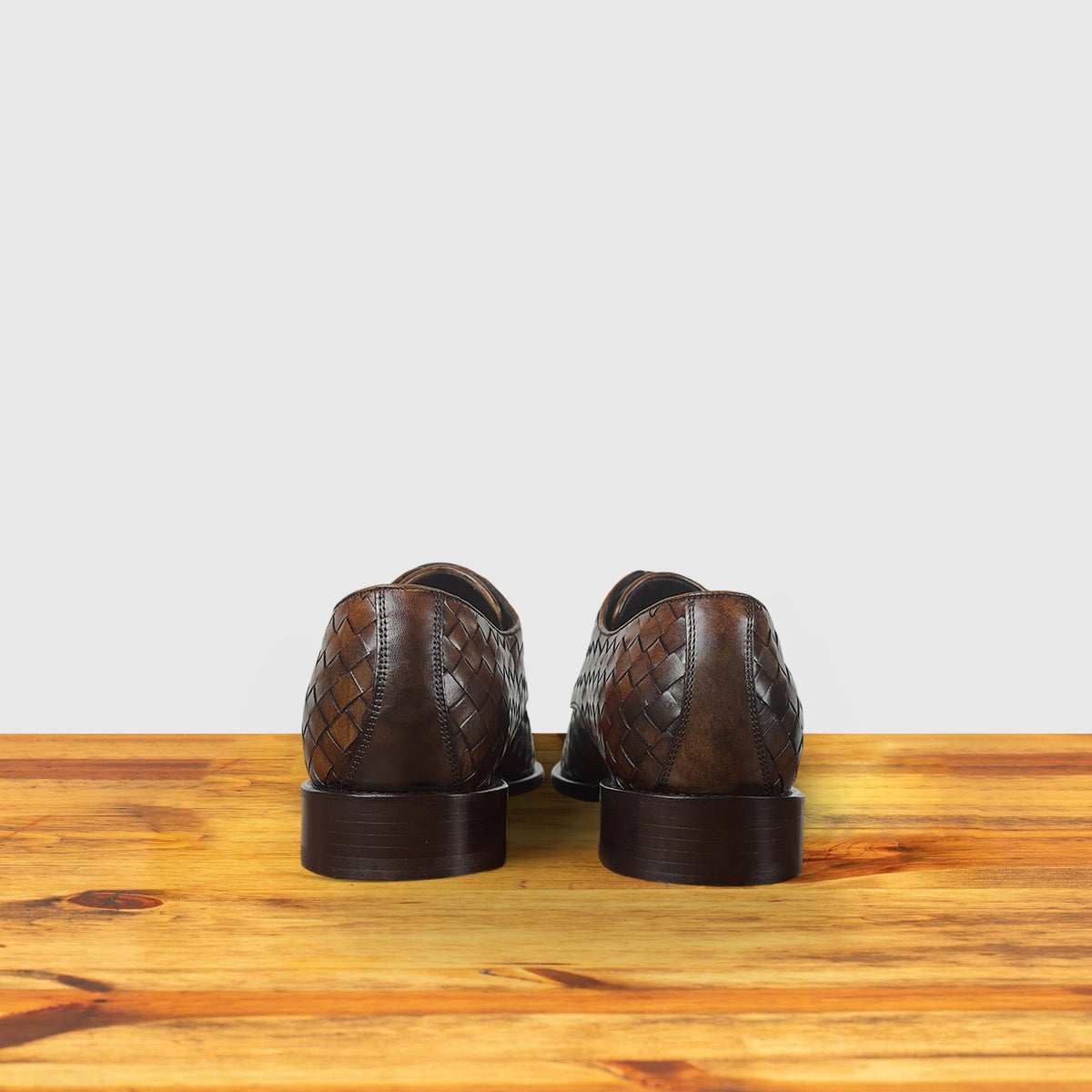 Pair of Mahogany leather shoes on a wooden surface with a light gray background