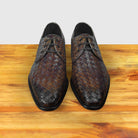 Pair of Mahogany woven leather shoes on a wooden surface with a light gray background