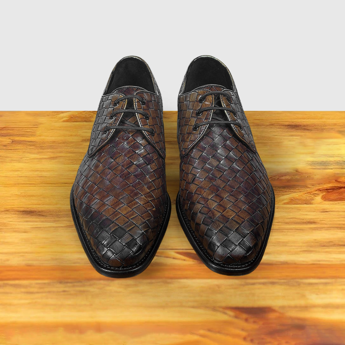 Pair of Mahogany woven leather shoes on a wooden surface with a light gray background
