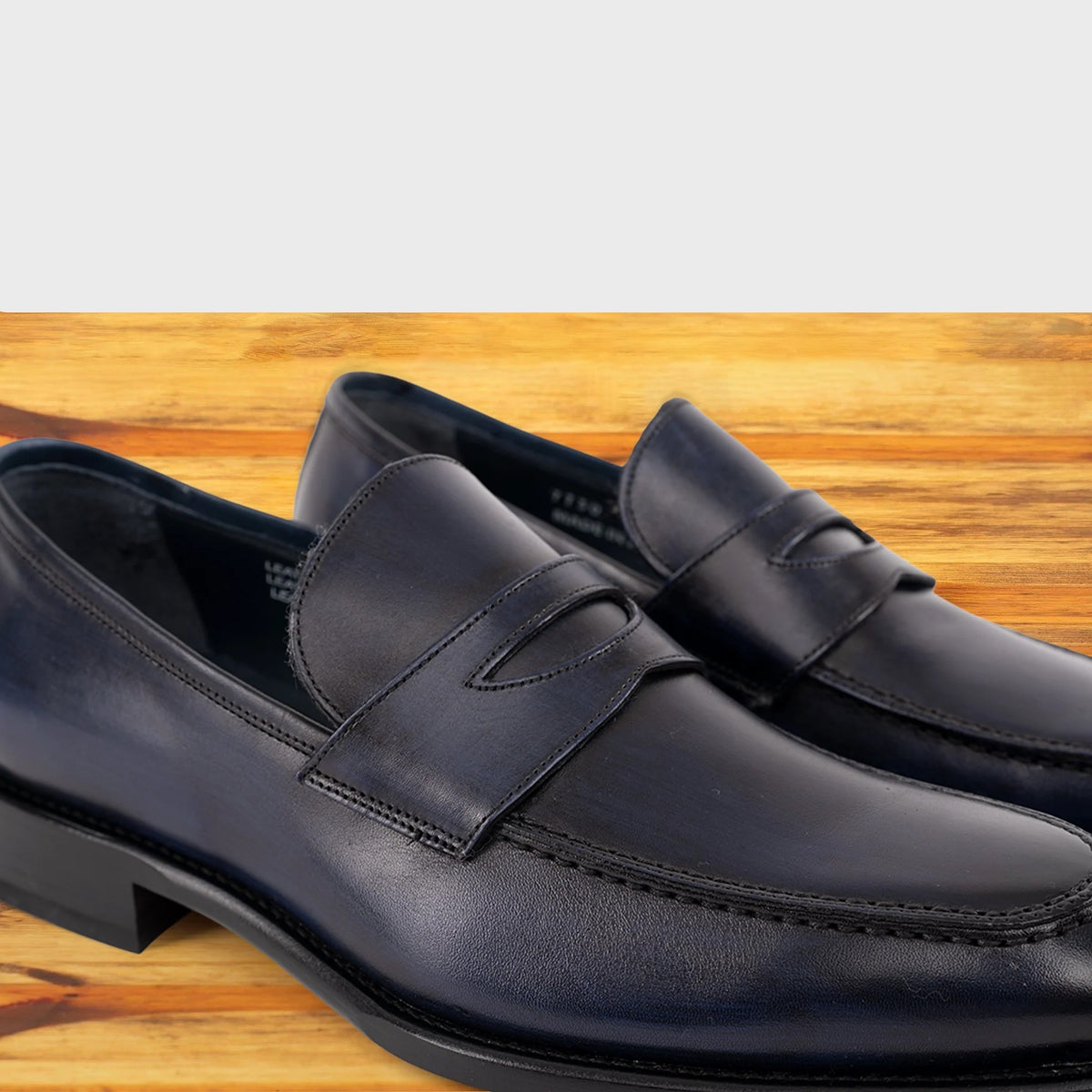 A Pair of navy blue Italian leather dress loafer with a penny strap, on a wooden surface.