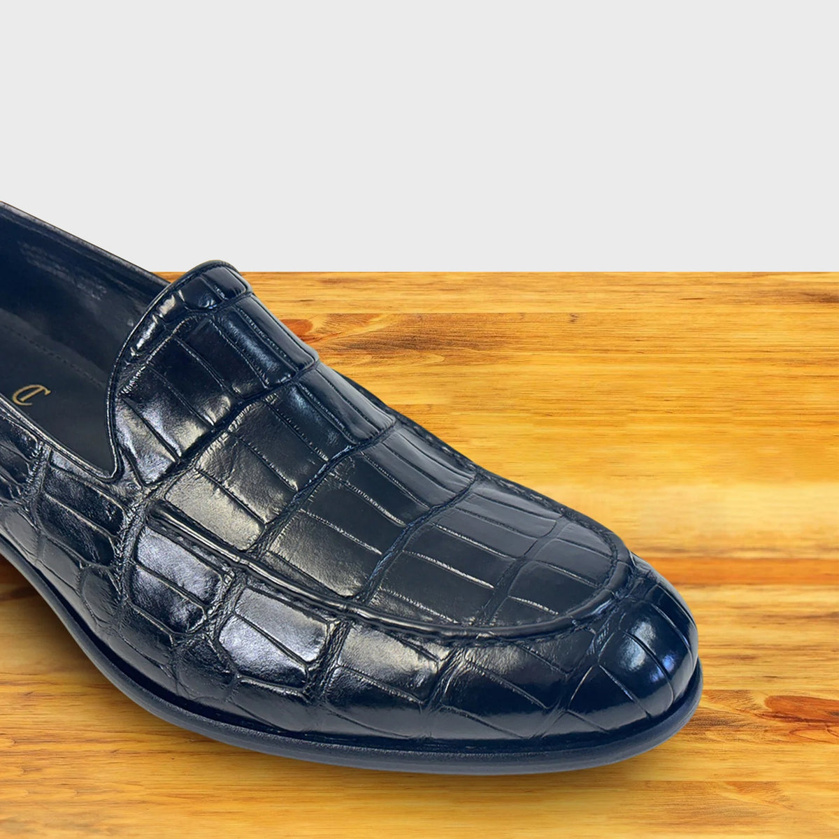 Black crocodile loafer shoe on a wooden surface.