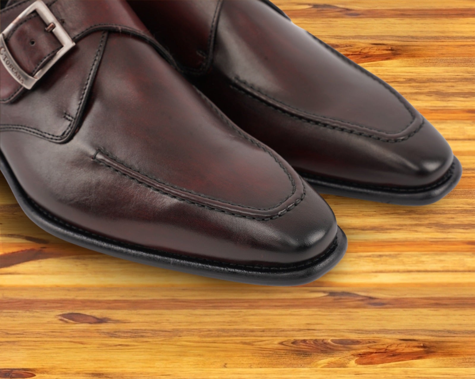 A close view of burgundy monk strap shoe with a silver buckle on a wooden surface