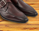 A close view of burgundy monk strap shoe with a silver buckle on a wooden surface